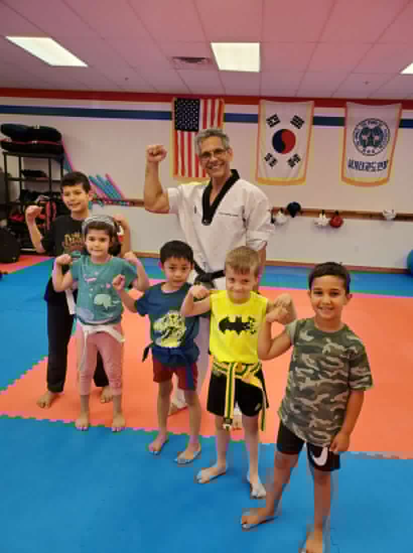 Five smiling kids flexing their muscles with Master Gonzalez in the dojang